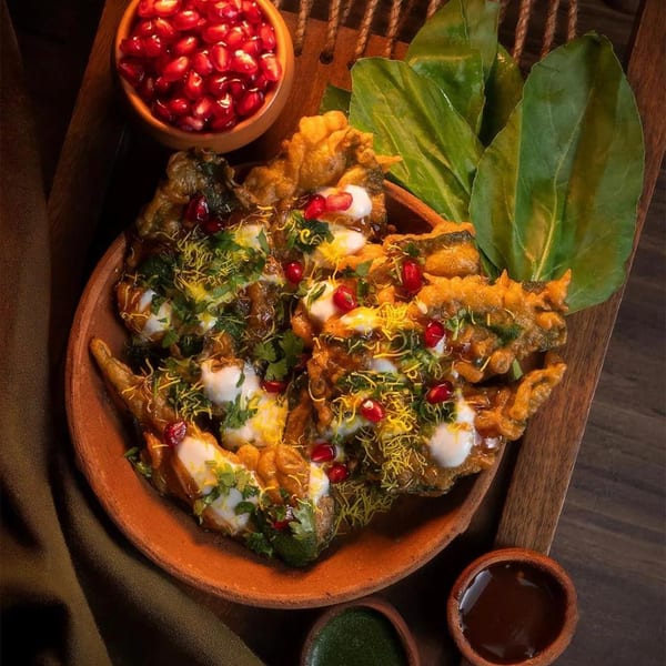 Crispy fried spinach pakoras topped with yogurt, chutneys, pomegranate, and sev, served with dipping sauces.