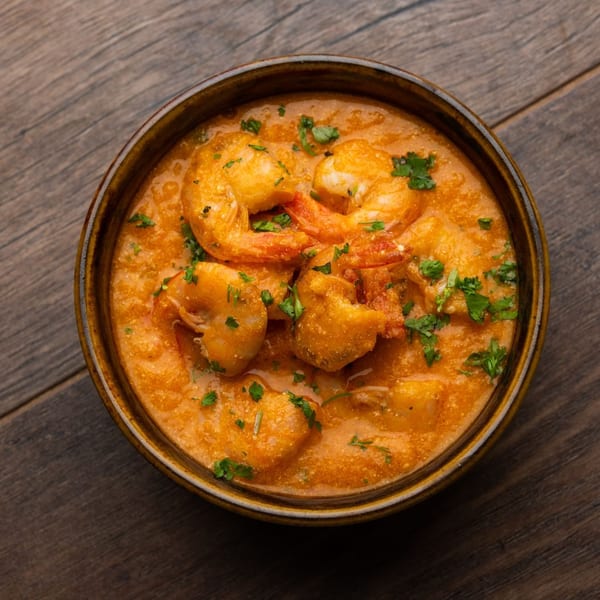 A vibrant orange shrimp curry, garnished with fresh green herbs, served in a brown bowl on wood.